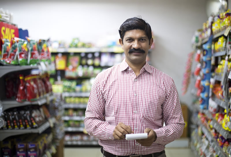 StoreManager-Powering_down_electronics A man holding a notepad stands in aisle of a convenience store.