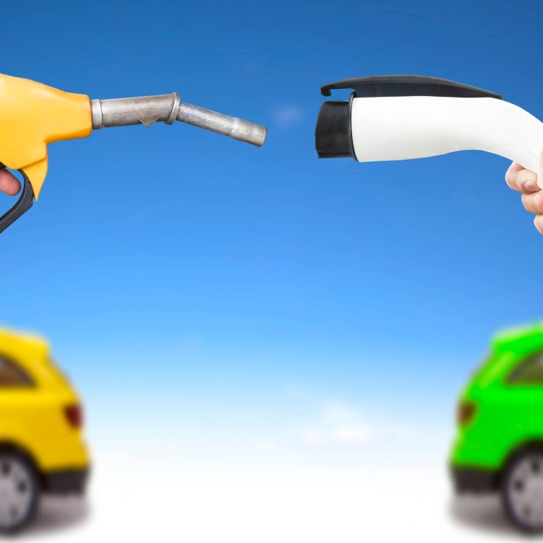 A hand holding a gasoline pump nozzle faces another hand that holds an electric vehicle charging port.